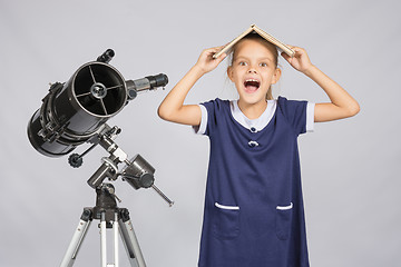 Image showing Schoolgirl covered her head with a textbook and cry looking at the frame, standing at the telescope