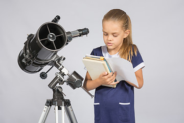 Image showing Schoolgirl reading a textbook while standing astronomer at the telescope