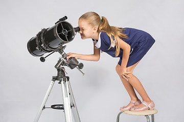 Image showing Seven-year girl standing on a chair and looks ridiculous in the eyepiece of the telescope reflector