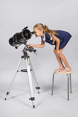 Image showing The young astronomer standing on a chair and funny looking in a telescope eyepiece