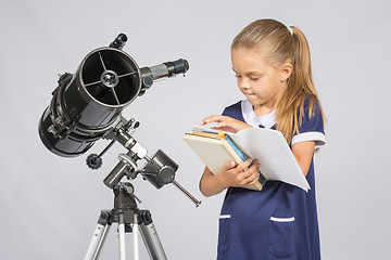 Image showing Schoolgirl astronomer leafing through books to find the right information at the stand of the telescope