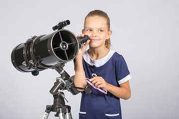 Image showing Seven-year girl standing next to a reflector telescope and looks mysteriously into the sky