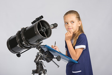 Image showing Seven-year girl thoughtful looking at the sky, making the recording of observations in the telescope