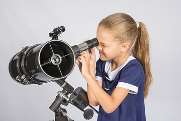 Image showing Seven-year girl squinting with interest looks in a reflector telescope