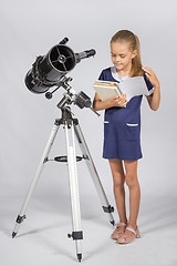 Image showing Schoolgirl leafing through a textbook while standing at the telescope