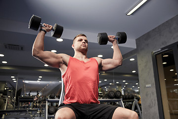 Image showing young man with dumbbells flexing muscles in gym