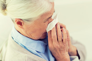 Image showing sick senior woman blowing nose to paper napkin