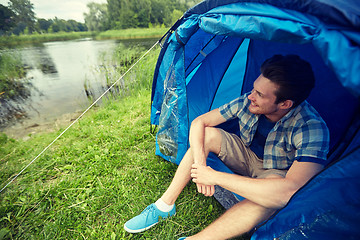 Image showing happy young man sitting in tent at camping