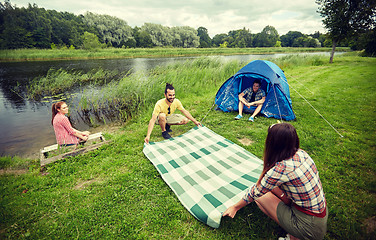 Image showing happy friends laying picnic blanket at campsite