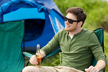 Image showing happy young man drinking beer at campsite tent