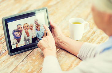 Image showing senior woman with family photo on tablet pc screen