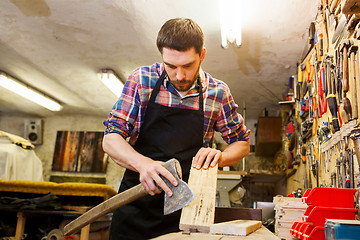 Image showing carpenter with ax and board working at workshop