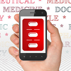 Image showing Health concept: Hand Holding Smartphone with Pills Blister on display