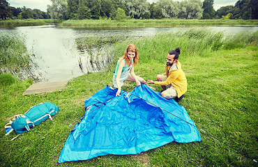 Image showing happy couple setting up tent outdoors