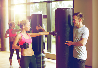 Image showing smiling woman with personal trainer boxing in gym