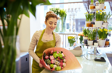 Image showing smiling florist woman packing bunch at flower shop