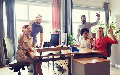 Image showing happy creative team waving hands in office