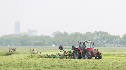 Image showing Farmer uses tractor to spread hay on the field