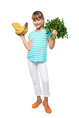 Image showing Smiling little girl holding fresh parsley and bananas