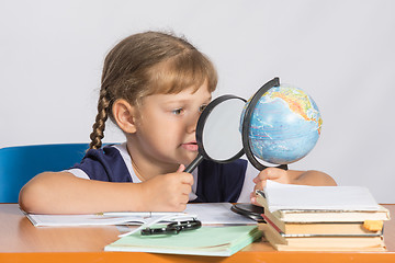 Image showing Six-year girl sitting at the table and looks at the globe through a magnifying glass