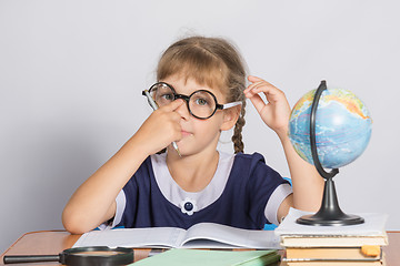 Image showing Schoolgirl corrects glasses while sitting at a desk in the classroom Geography