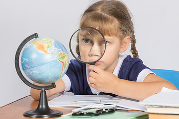 Image showing Schoolgirl looking at globe through a magnifying glass