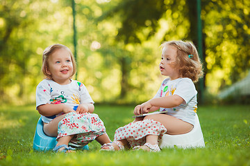 Image showing The two little baby girls sitting on pots