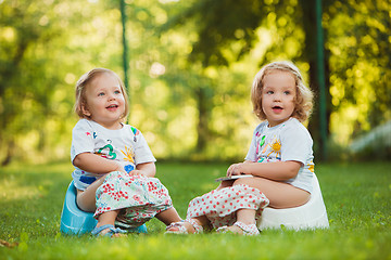 Image showing The two little baby girls sitting on pots