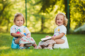 Image showing The two little baby girls sitting on pots