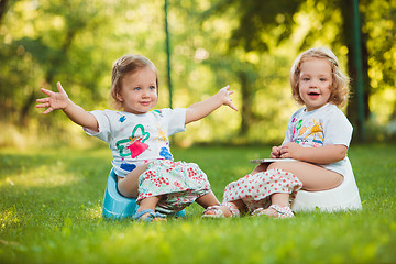 Image showing The two little baby girls sitting on pots