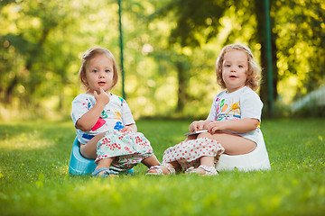 Image showing The two little baby girls sitting on pots