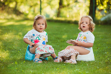 Image showing The two little baby girls sitting on pots