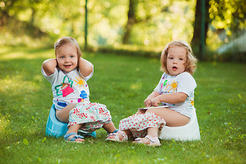 Image showing The two little baby girls sitting on pots