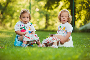 Image showing The two little baby girls sitting on pots