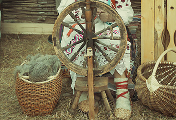 Image showing An elderly woman spinning thread on a spinning wheel.