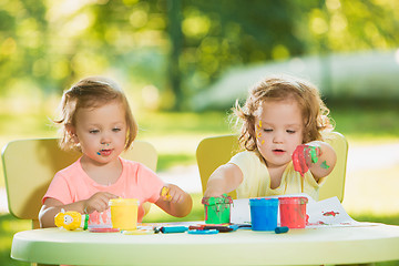 Image showing Two-year old girls painting with poster paintings together against green lawn