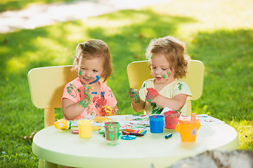 Image showing Two-year old girls painting with poster paintings together against green lawn