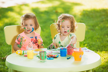 Image showing Two-year old girls painting with poster paintings together against green lawn