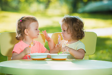 Image showing Two little girls sitting at a table and eating together against green lawn