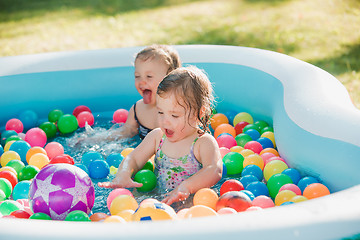 Image showing The two little baby girls playing with toys in inflatable pool in the summer sunny day