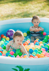 Image showing The two little baby girls playing with toys in inflatable pool in the summer sunny day