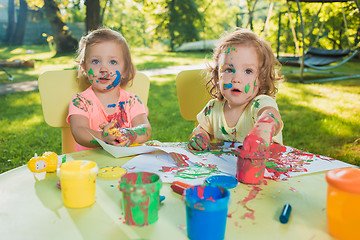 Image showing Two-year old girls painting with poster paintings together against green lawn