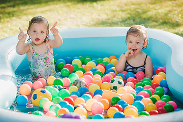 Image showing The two little baby girls playing with toys in inflatable pool in the summer sunny day