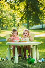 Image showing Two little girls sitting at a table and eating together against green lawn