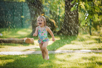 Image showing The little baby girl playing with garden sprinkler.