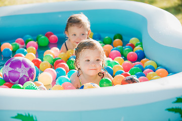 Image showing The two little baby girls playing with toys in inflatable pool in the summer sunny day