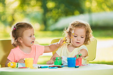 Image showing Two-year old girls painting with poster paintings together against green lawn