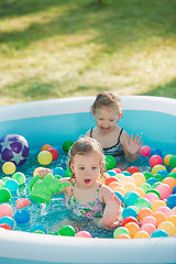 Image showing The two little baby girls playing with toys in inflatable pool in the summer sunny day