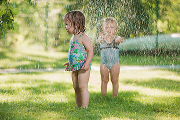 Image showing The two little baby girls playing with garden sprinkler.