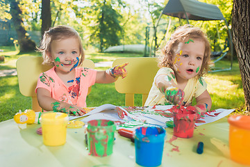 Image showing Two-year old girls painting with poster paintings together against green lawn